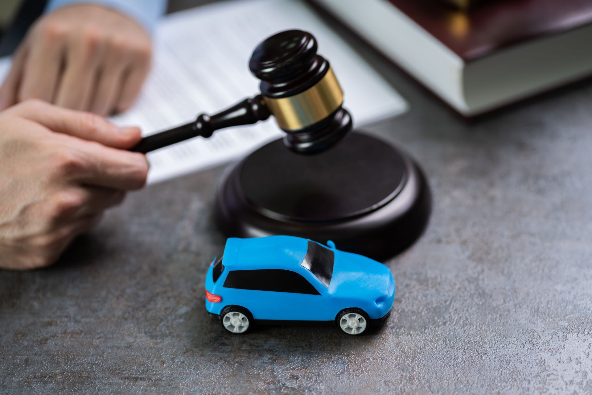 Hand with gavel beside blue toy car, suggesting an insurance or legal claim scene