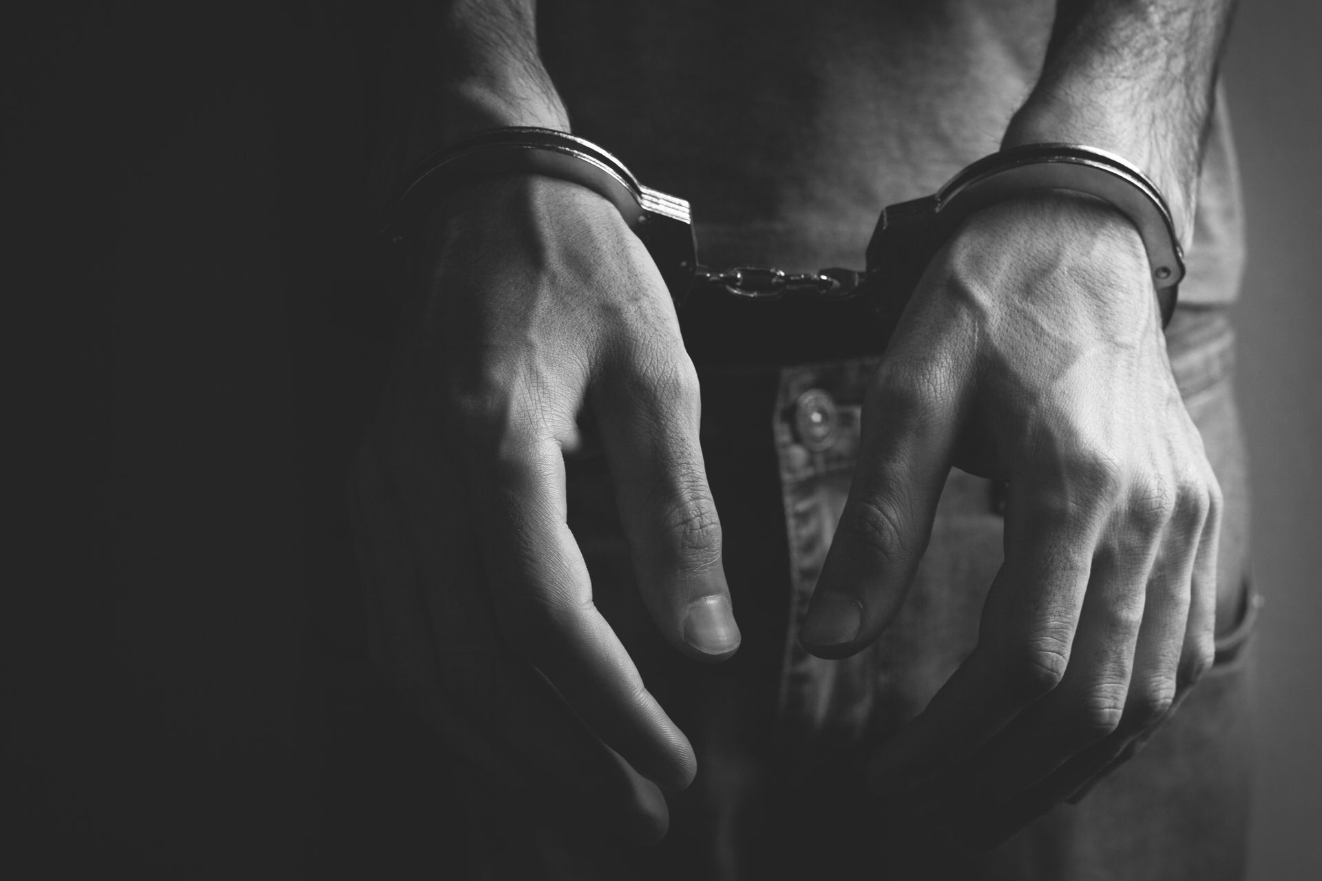 Hands in handcuffs; torso visible. Black and white.