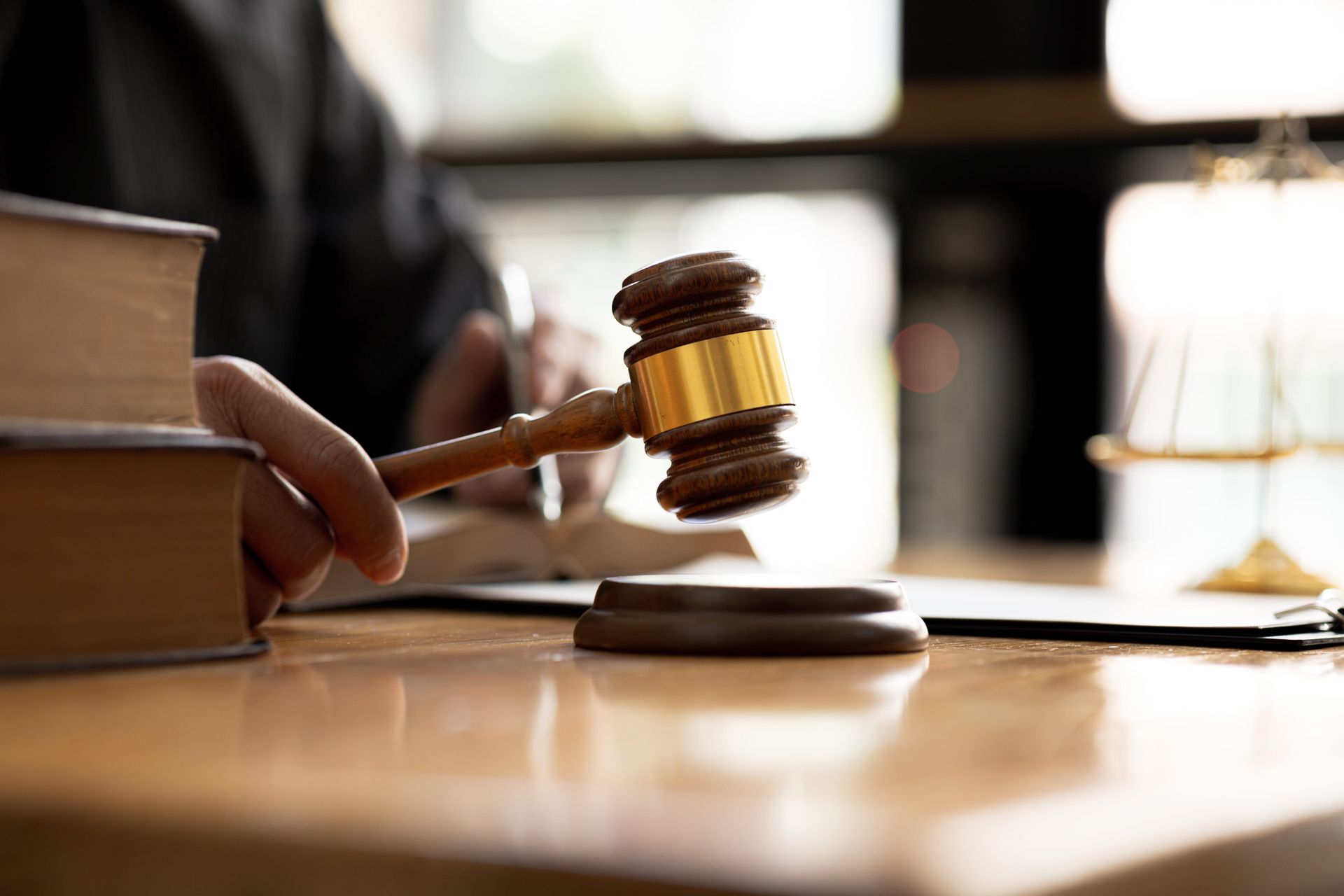 Judge’s gavel poised over a desk in a courtroom, with stacked books nearby