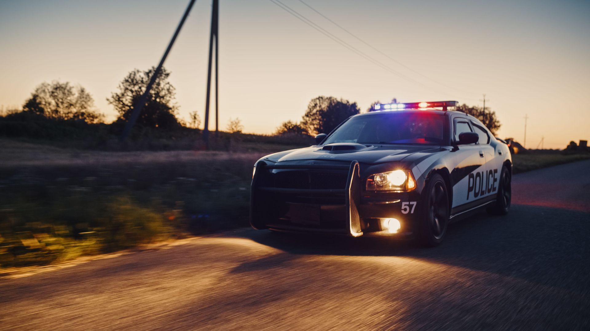 Police car with flashing lights driving on a rural road at sunset