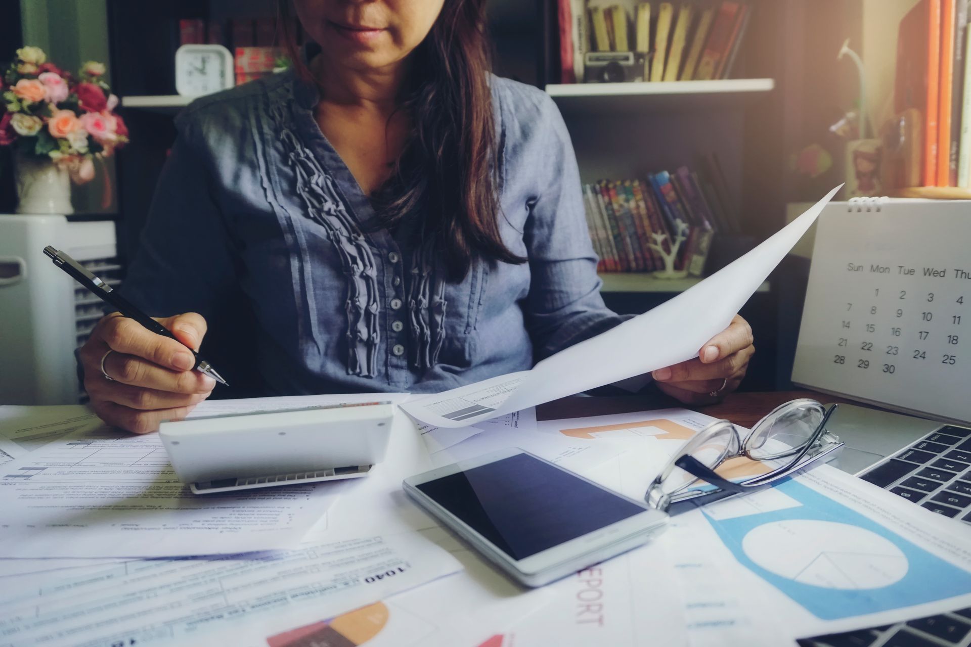 Person reviewing papers at a desk with a calculator, notebook, and calendar nearby.
