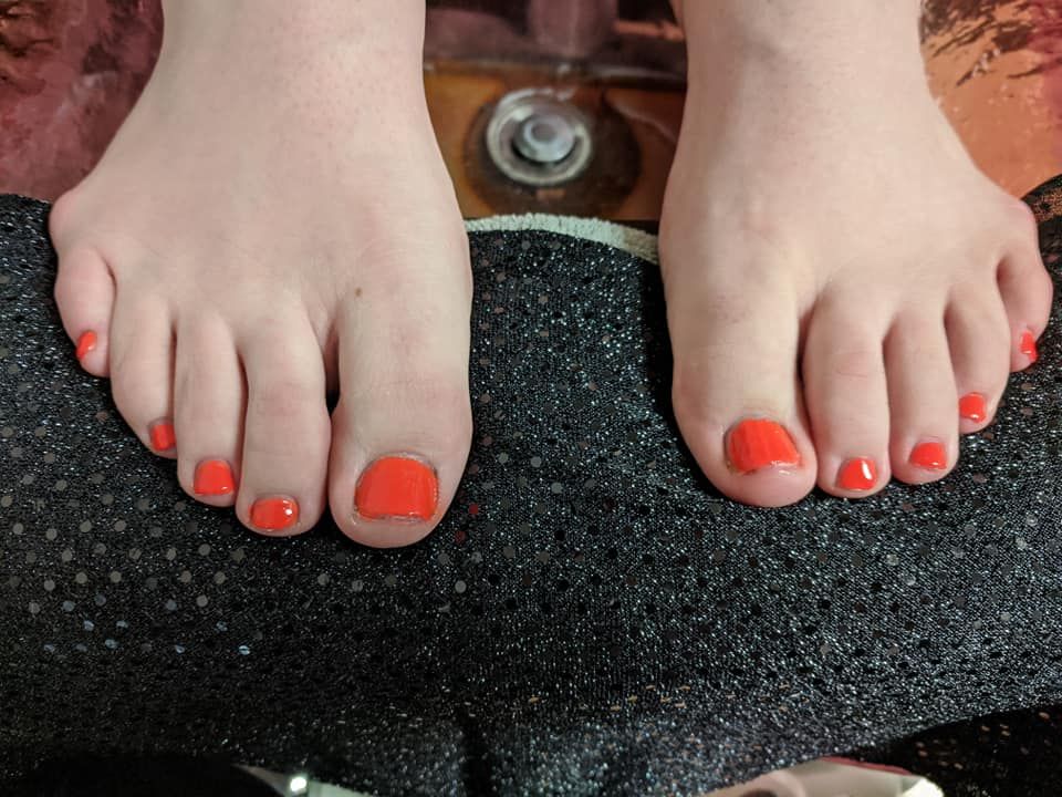 Bare feet with bright orange toenail polish resting on a textured black mat