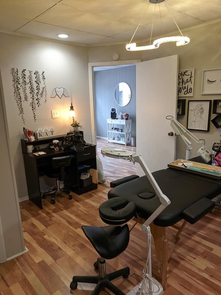 Small home salon with styling chair, black worktable, mirror, lamp, and framed wall art on hardwood floors.