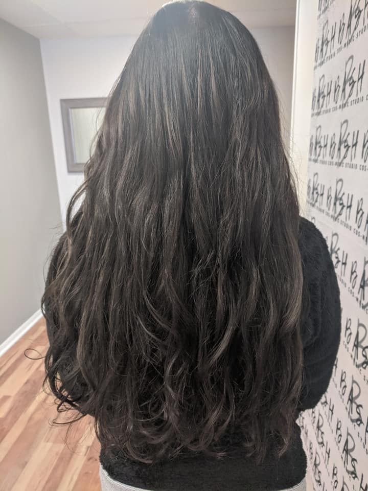 Back view of long wavy dark hair in a hallway with patterned wallpaper and wood floors
