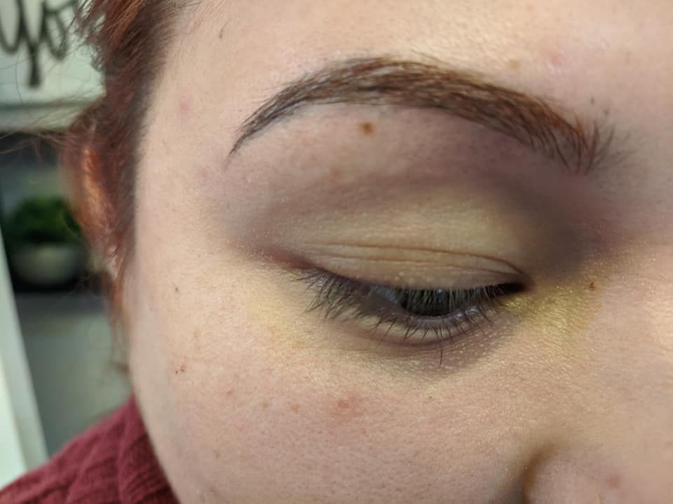 Close-up of a closed eye with a small mole on the forehead and a red sweater collar.