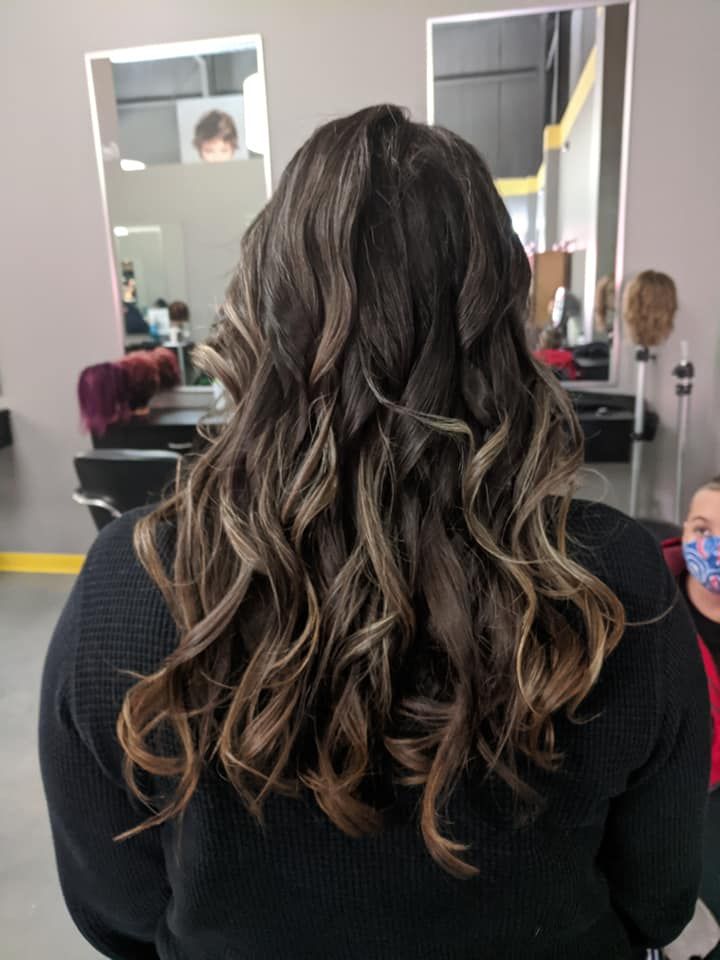 Long wavy brunette hair with blonde highlights seen from behind in a salon chair.