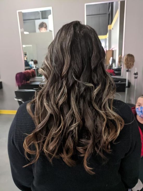 Wavy brown hair with blonde highlights styled in loose curls in a salon chair