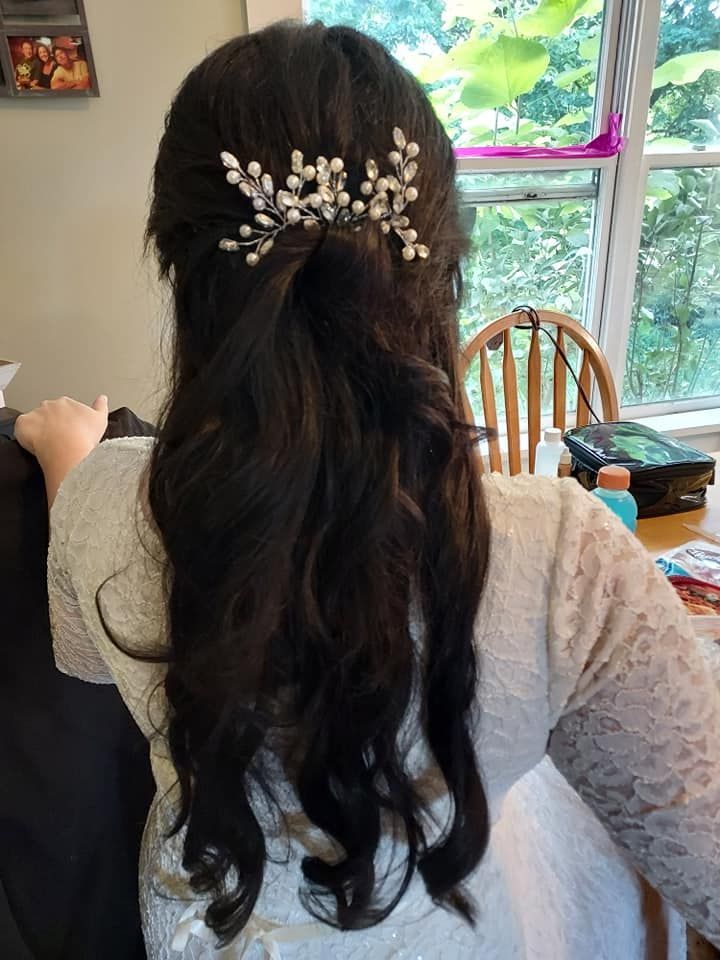 Woman with long dark hair and white floral hair clip, seen from behind in a bright room by a window.