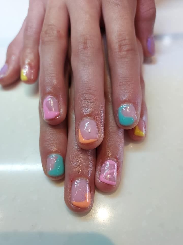 Hands with pastel rainbow nail art, including pink, teal, yellow, and glitter accents.