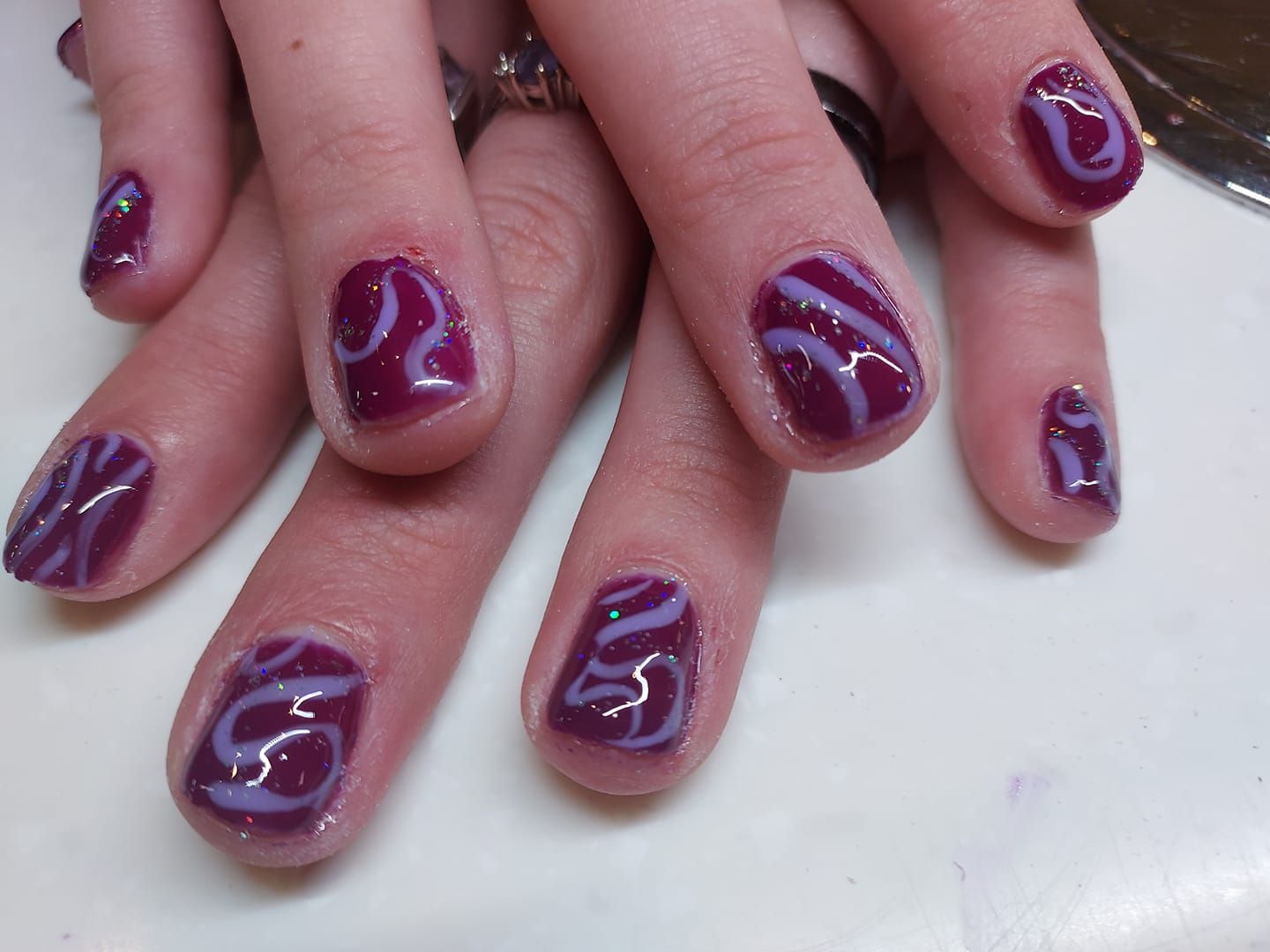 Close-up of hands with glossy purple nail art and white swirls on a light surface