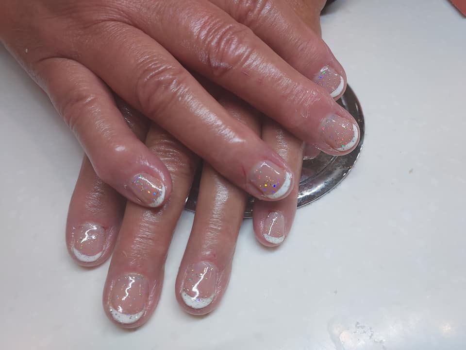 Hands with pink glittery manicure resting on a white surface.