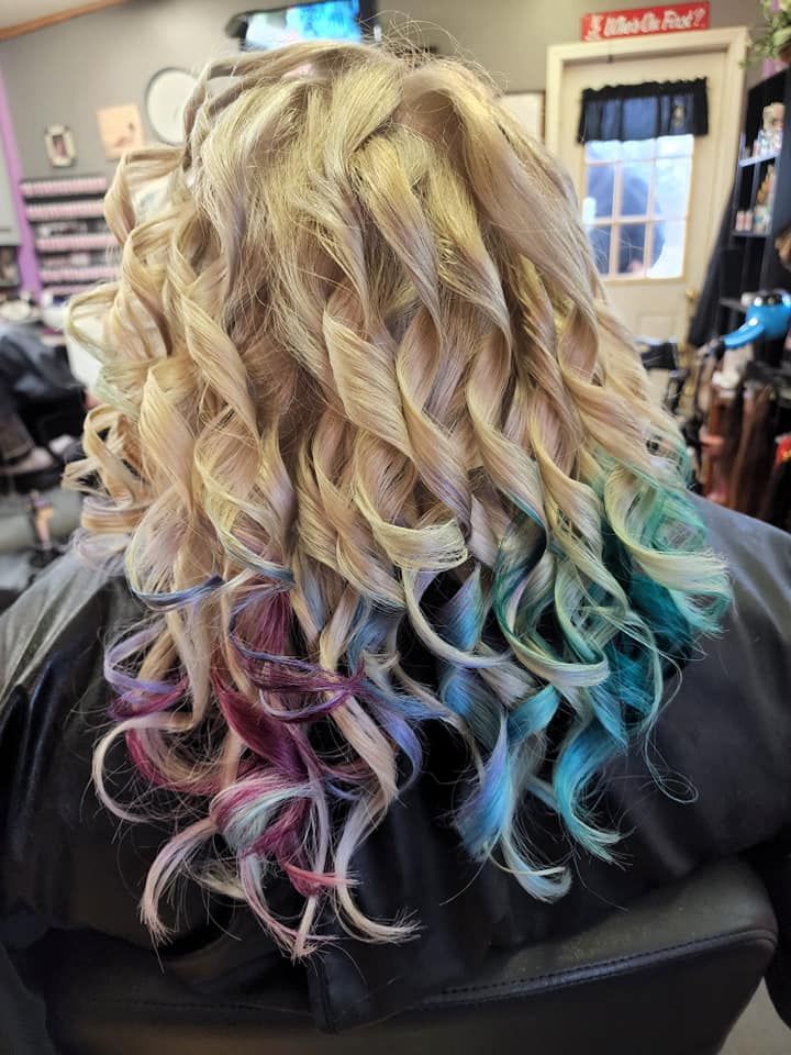 Curly blonde hair with pastel pink and blue highlights, viewed from behind in a salon chair