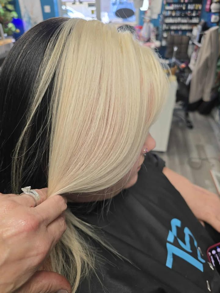 Stylist sectioning platinum blonde hair in a salon chair, with dark roots visible