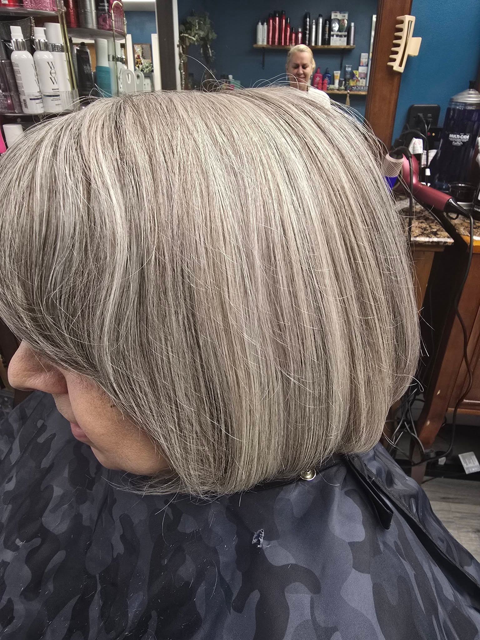 Close-up of a short blond bob haircut with dark roots in a salon chair, stylist in background