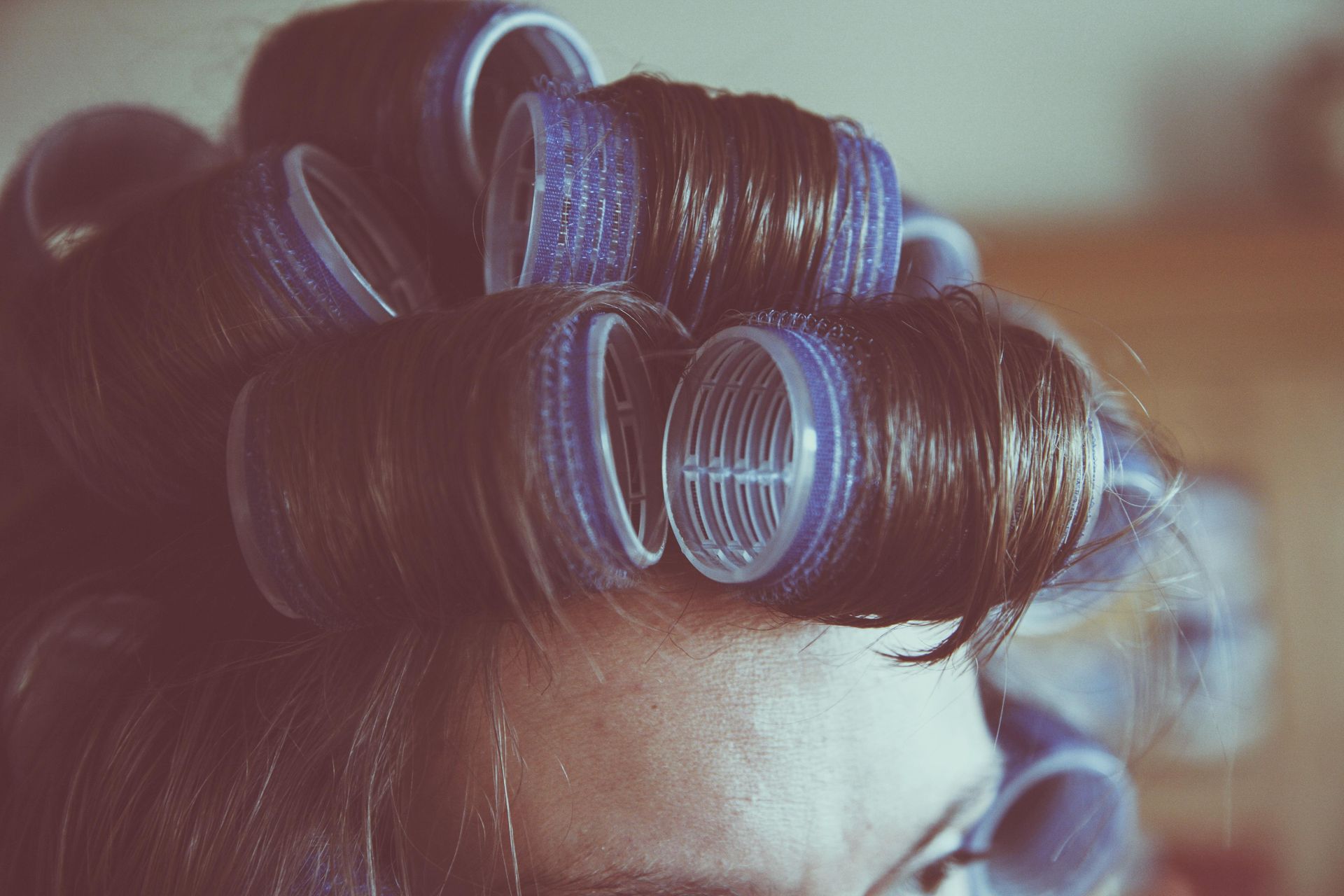 Close-up of blue hair rollers in dark hair, with a blurred indoor background.