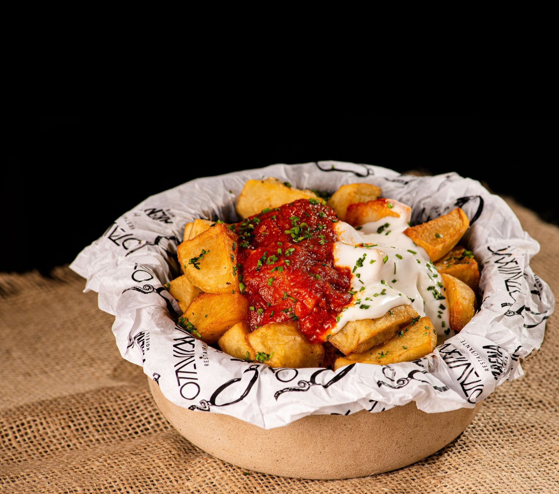Tigela de batatas fritas cobertas com molho vermelho e creme branco sobre papel manteiga.