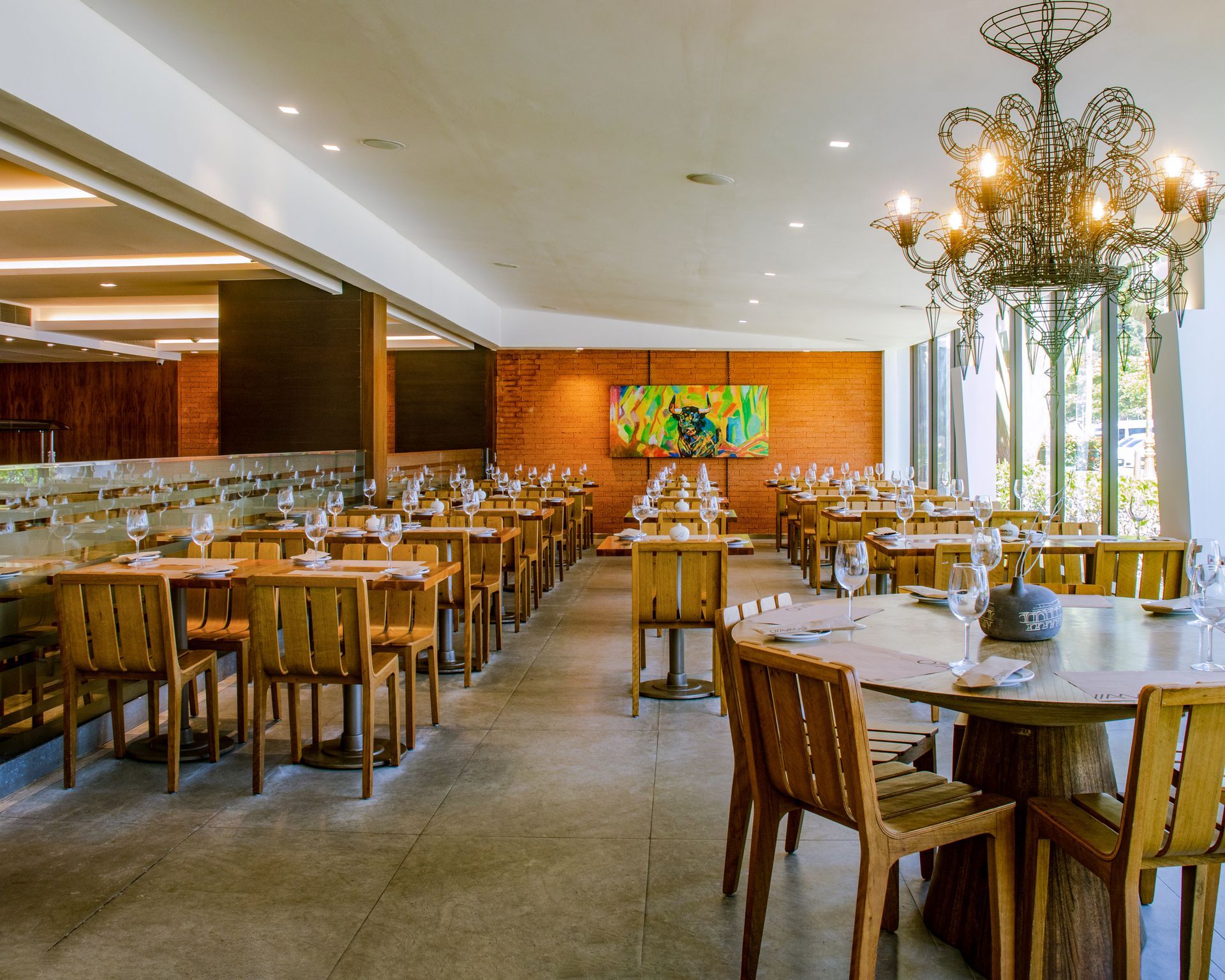 Sala de jantar elegante do restaurante com mesas de madeira, lustres e grandes janelas.