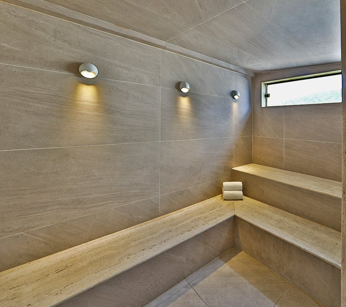 Sauna moderna de pedra com bancos embutidos, iluminação de parede e uma pequena janela.