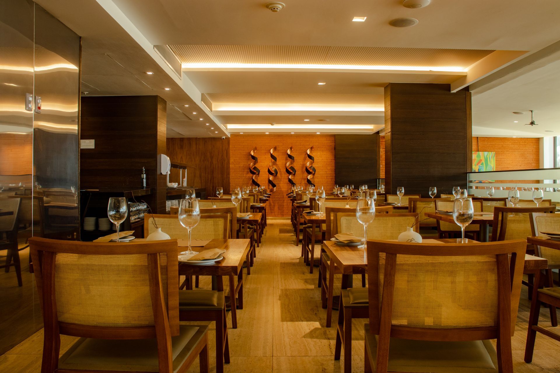Sala de jantar elegante de restaurante com mesas de madeira, iluminação aconchegante e talheres impecavelmente arrumados.
