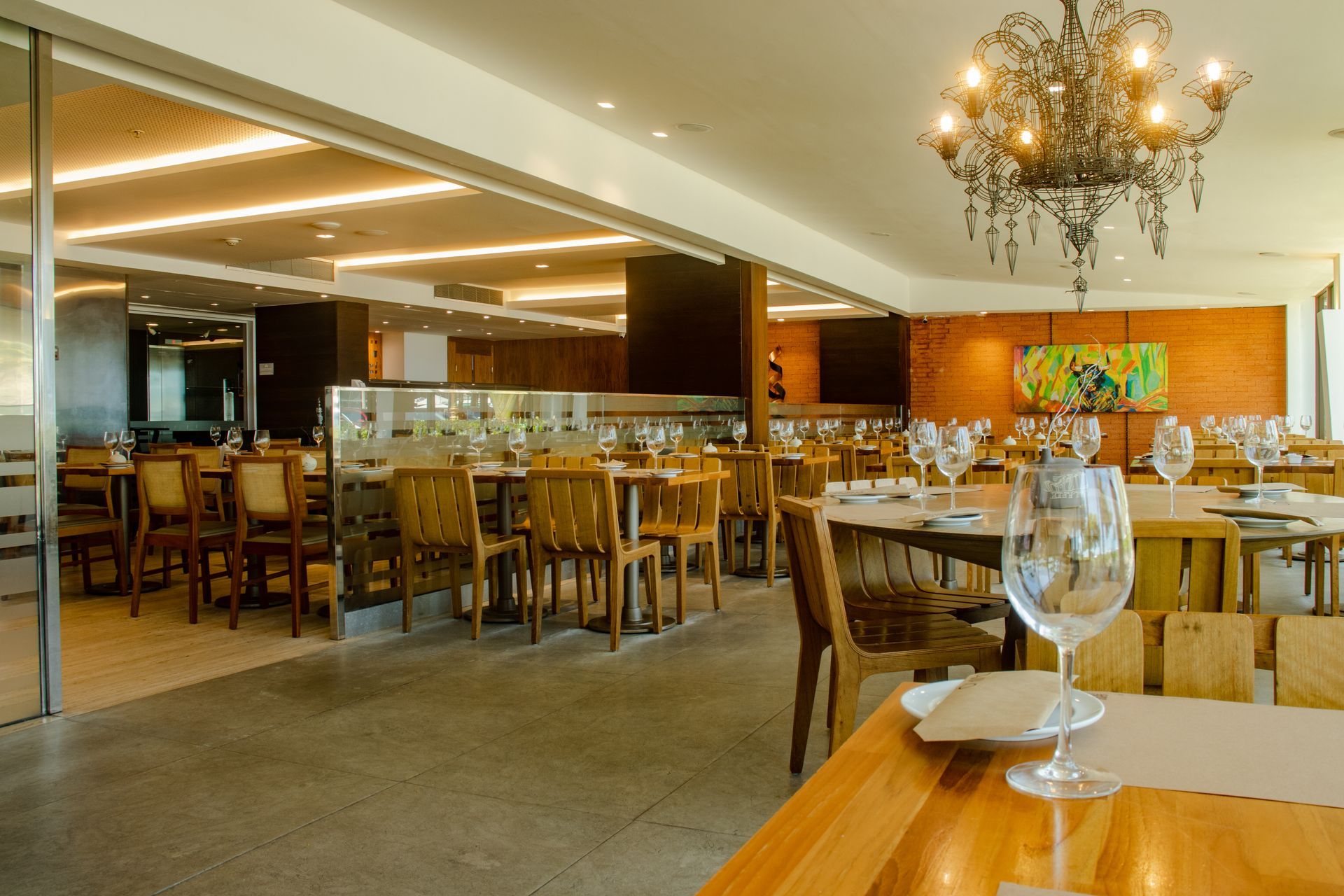 Sala de jantar moderna de restaurante com mesas de madeira, lustres e taças de vinho.