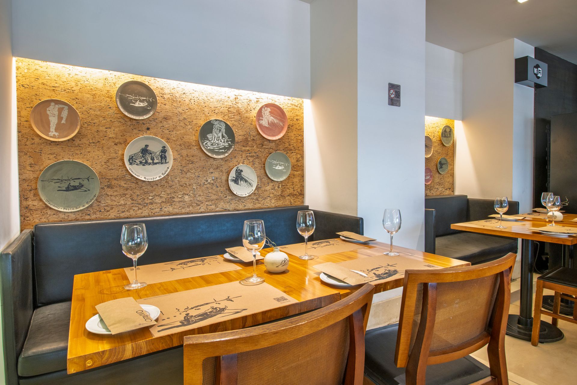 Cabine de jantar moderna de restaurante com mesa de madeira, conjunto de copos e pratos decorativos na parede.