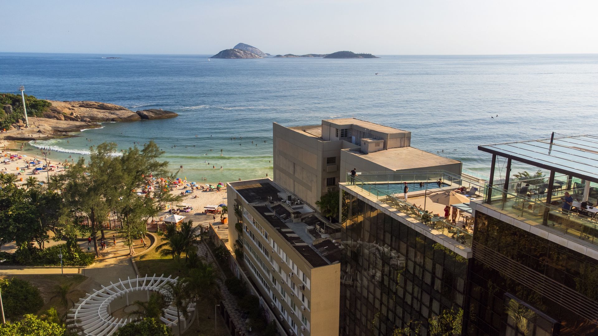 Resort costeiro com piscina, praia rochosa, mar turquesa e pequenas ilhas ao longe.