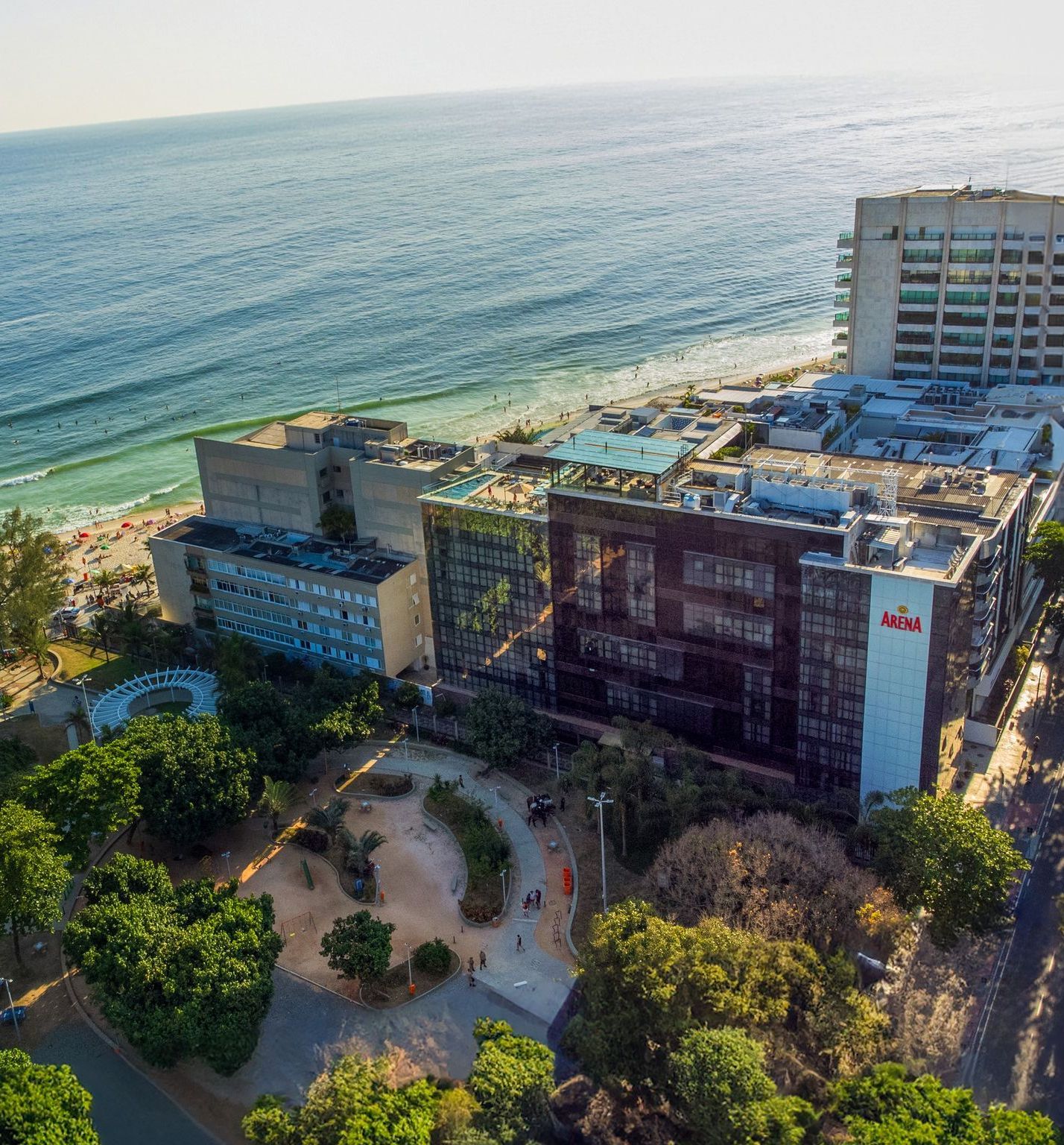 Edifícios de um resort costeiro junto a uma praia de areia e oceano turquesa, com árvores e um pátio circular em baixo.