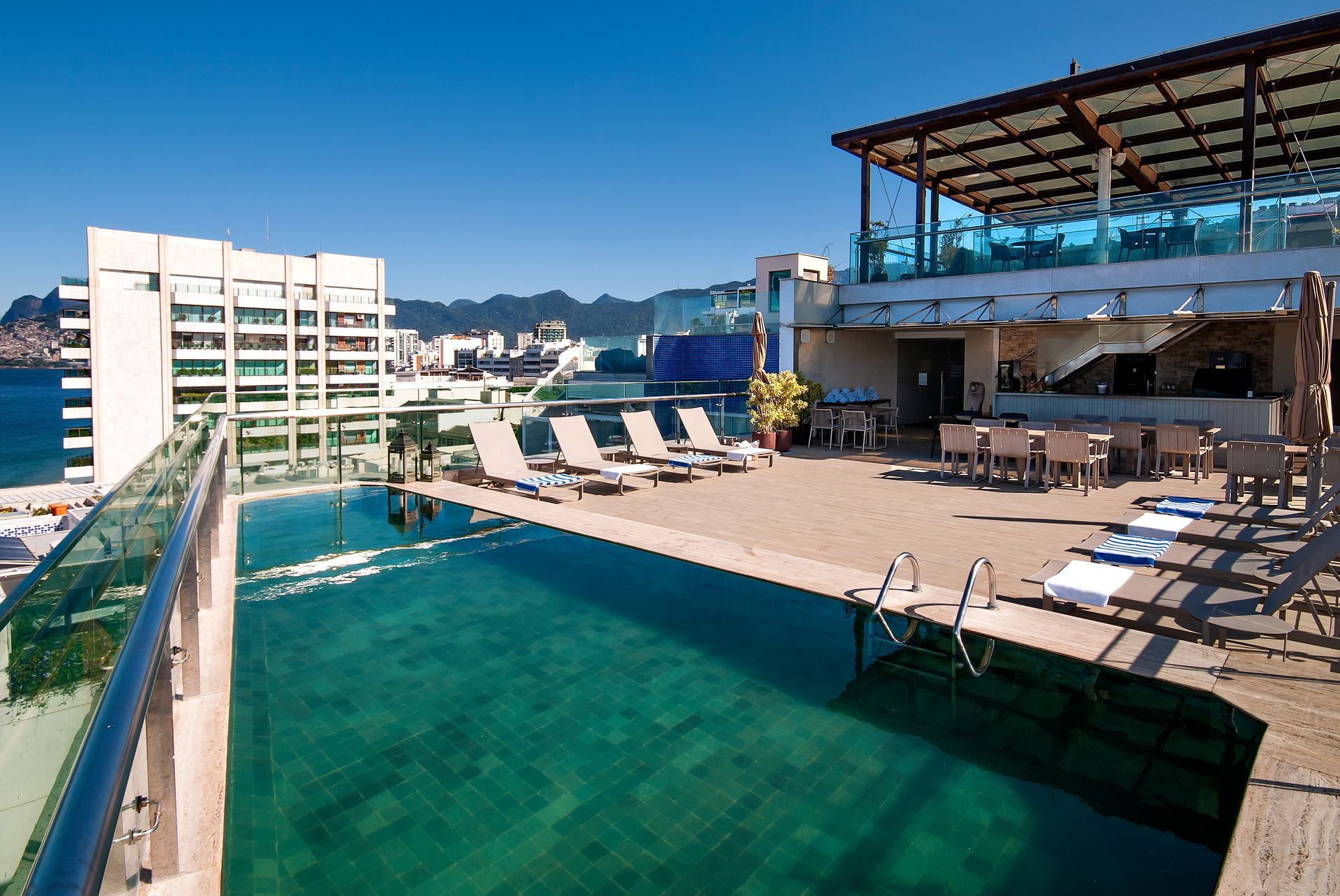 Piscina na cobertura com espreguiçadeiras e vista para a cidade sob um céu azul límpido.
