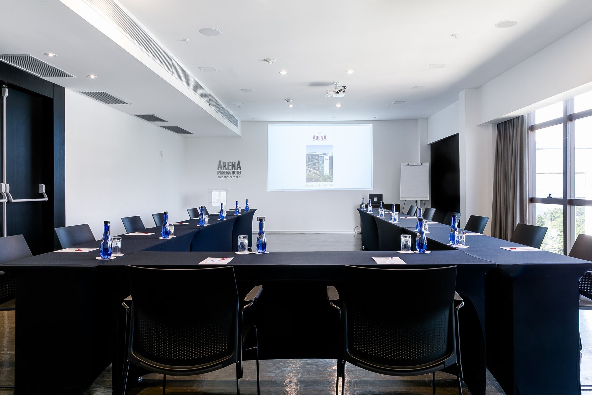 Sala de conferências moderna com uma mesa comprida, cadeiras azuis e uma tela de projeção.