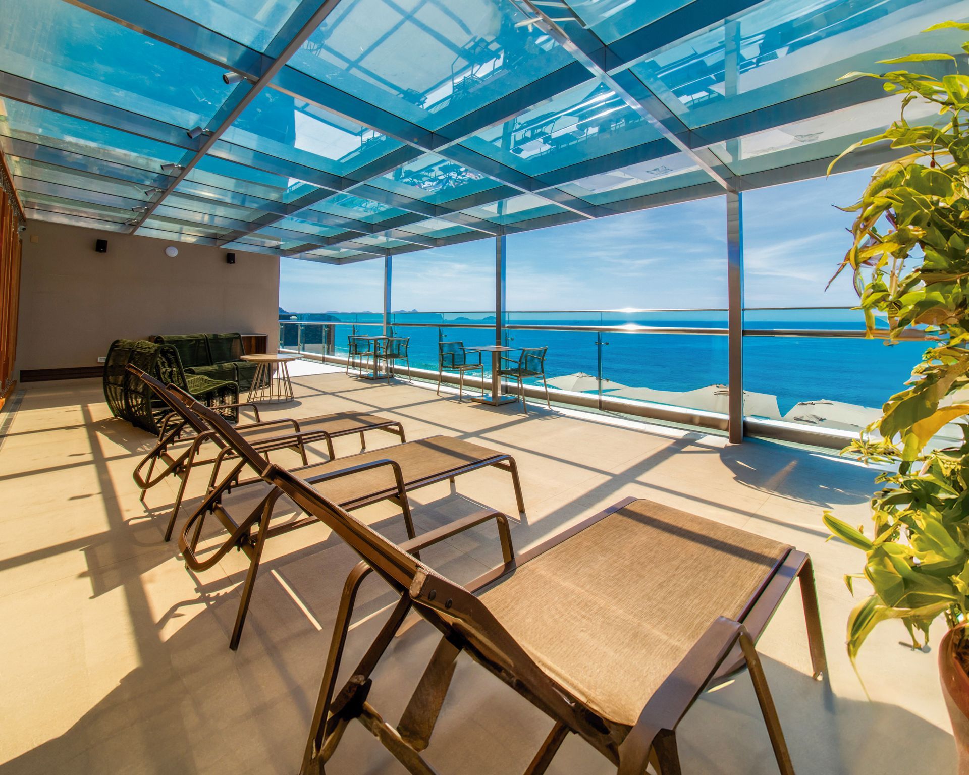 Terraço à beira-mar com espreguiçadeiras sob um teto de vidro, com vista para o oceano.