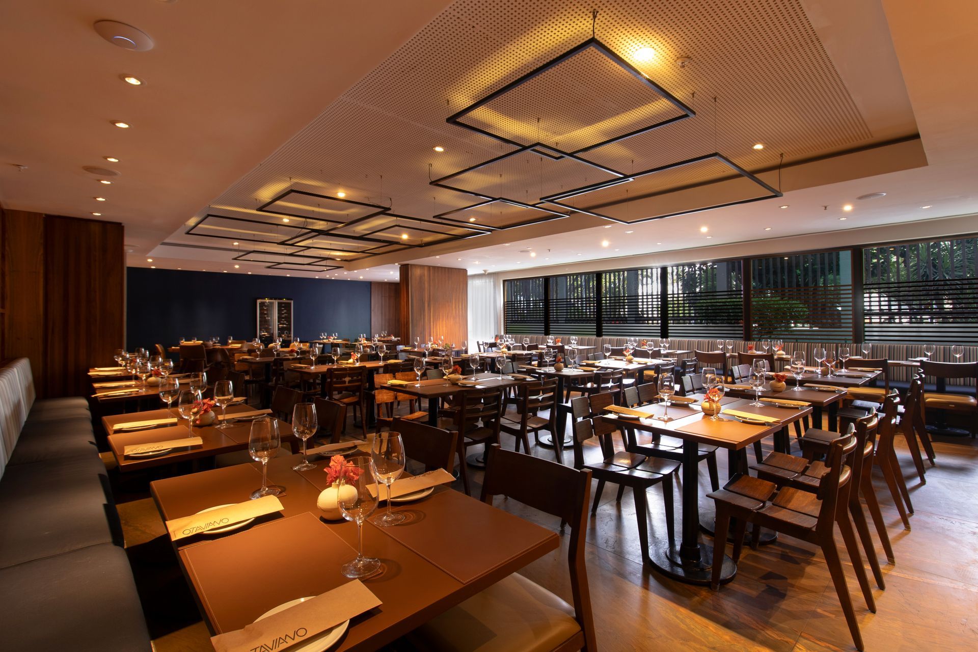 Sala de jantar de um restaurante moderno e vazio, com mesas cuidadosamente arrumadas e iluminação ambiente aconchegante.
