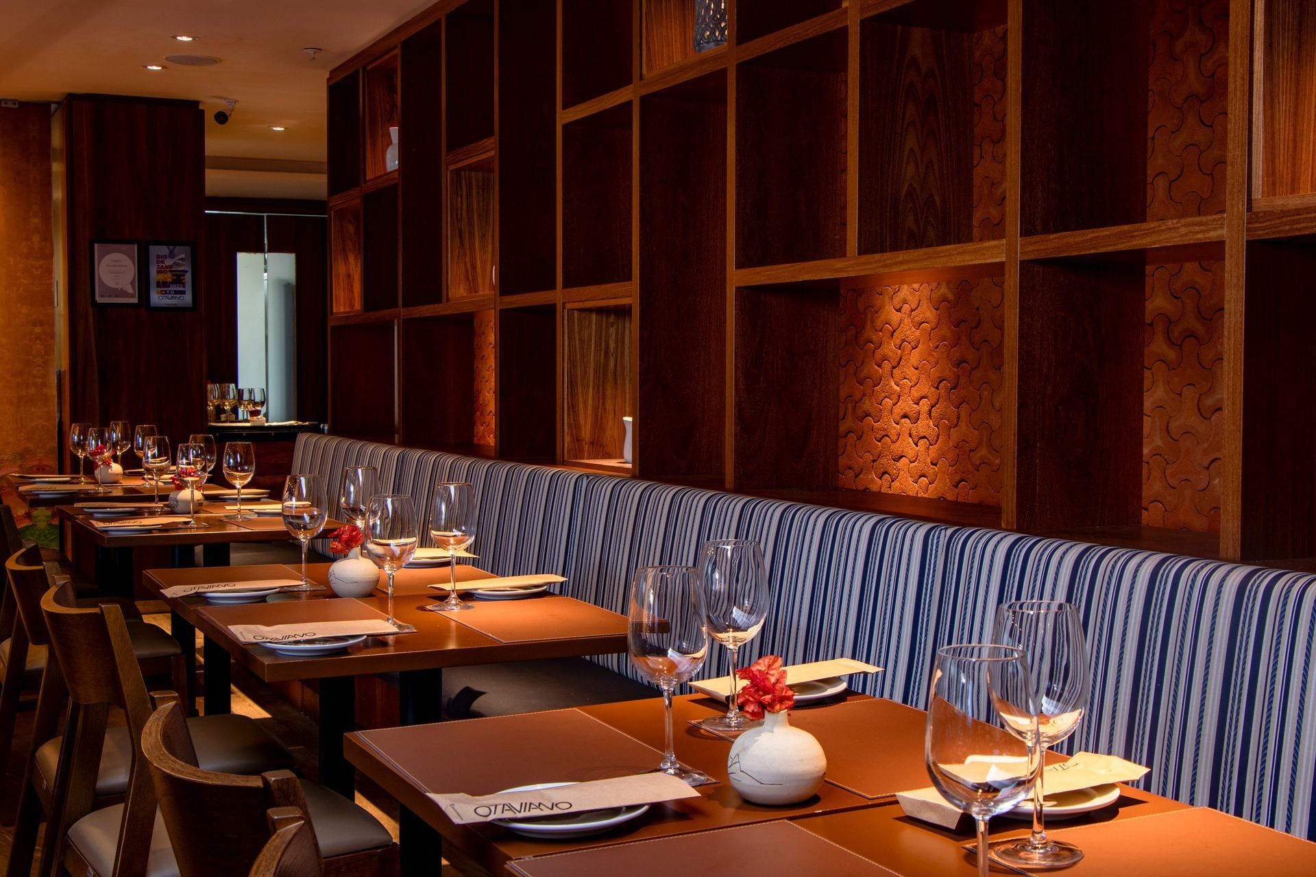 Sala de jantar vazia de um restaurante com mesas postas, iluminação aconchegante e cadeiras azuis estampadas encostadas na parede.