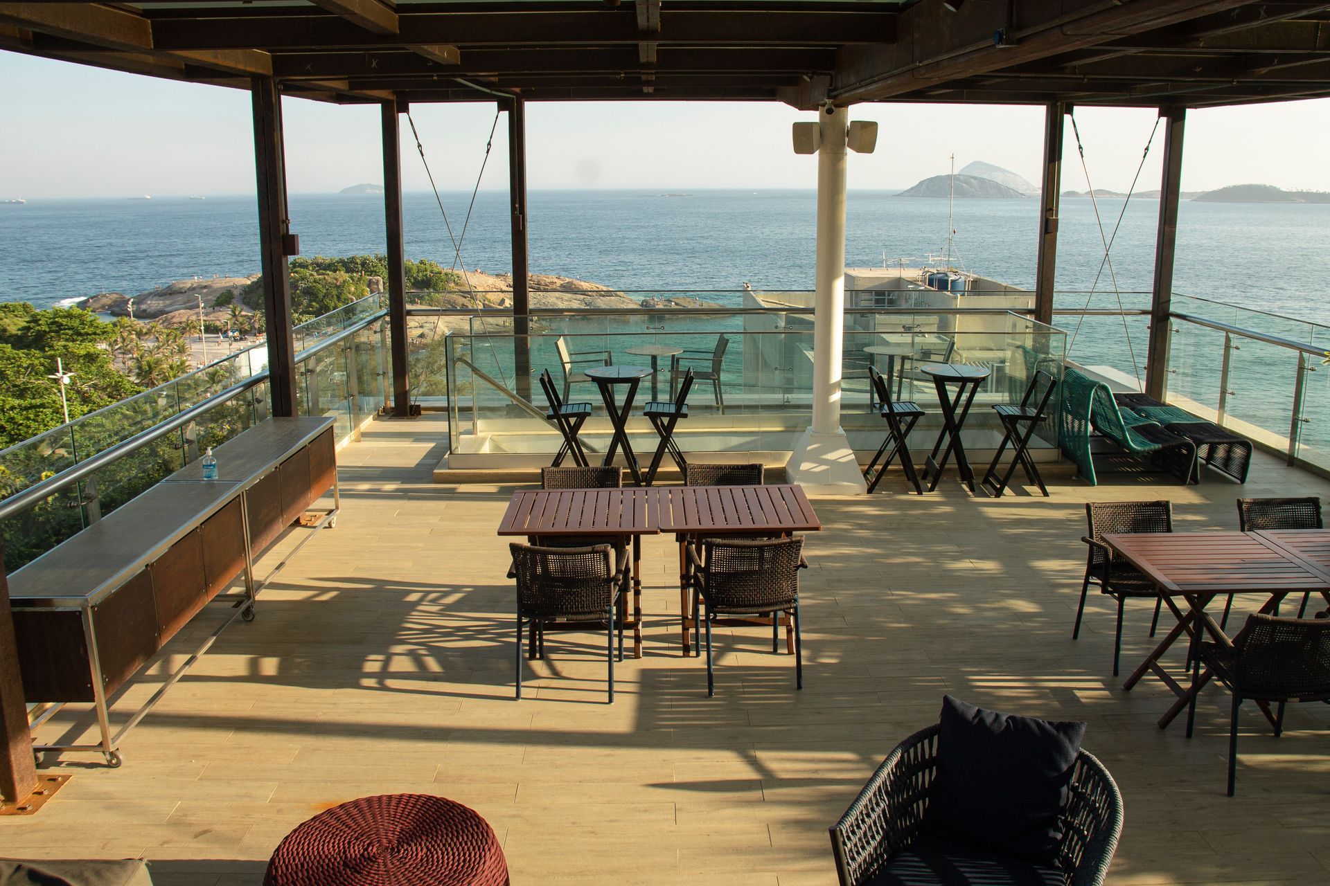 Terraço de café ao ar livre à beira-mar com mesas com vista para o oceano e uma ilha distante.