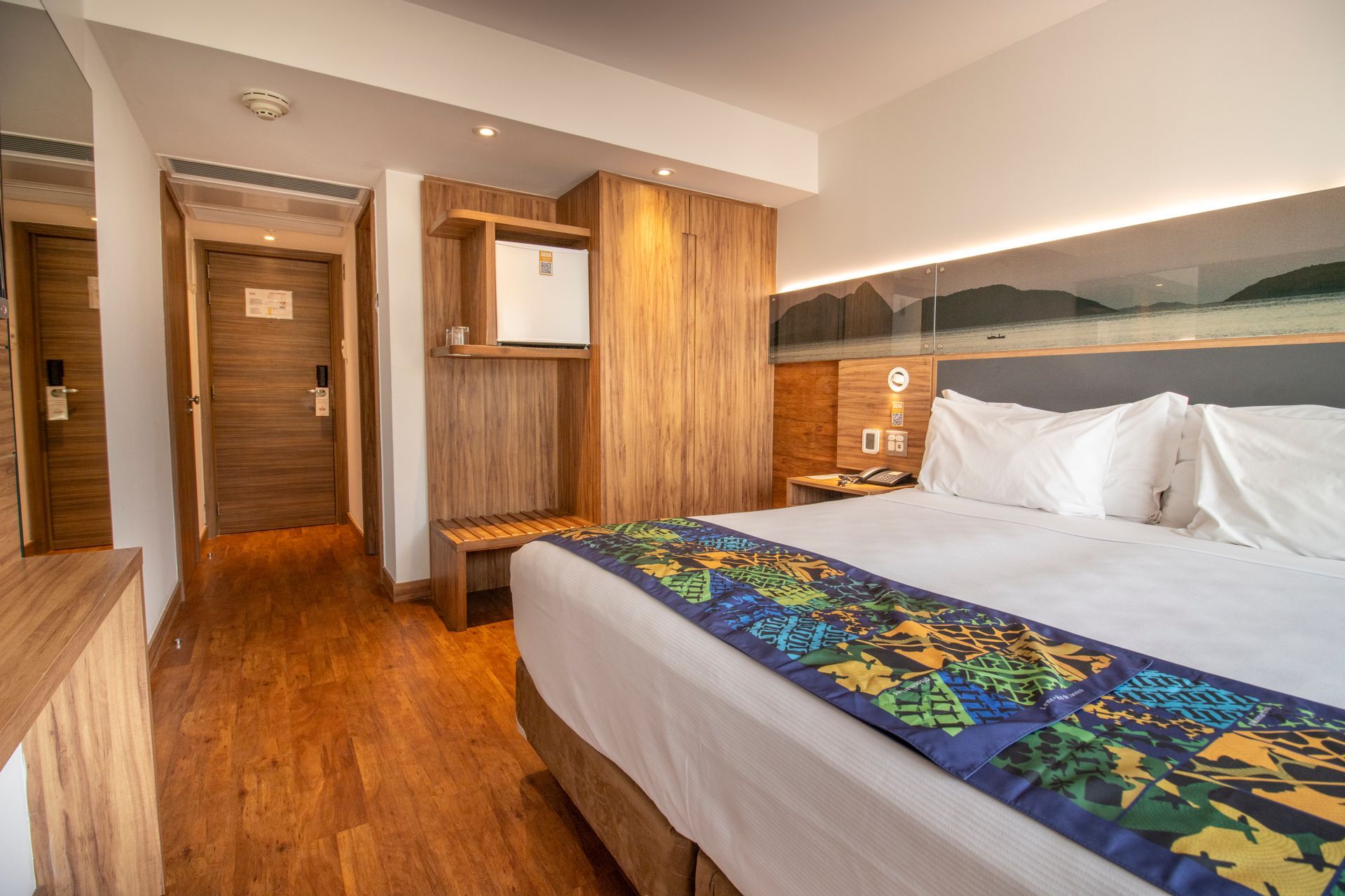 Quarto de hotel moderno com cama grande, piso de madeira e paredes revestidas de madeira em tons quentes.