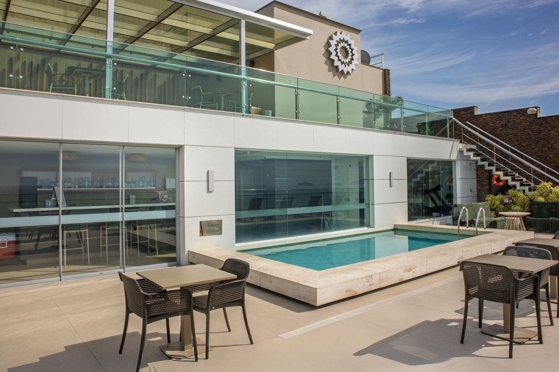 Terraço moderno com piscina na cobertura, espreguiçadeiras, paredes de vidro e escada externa.