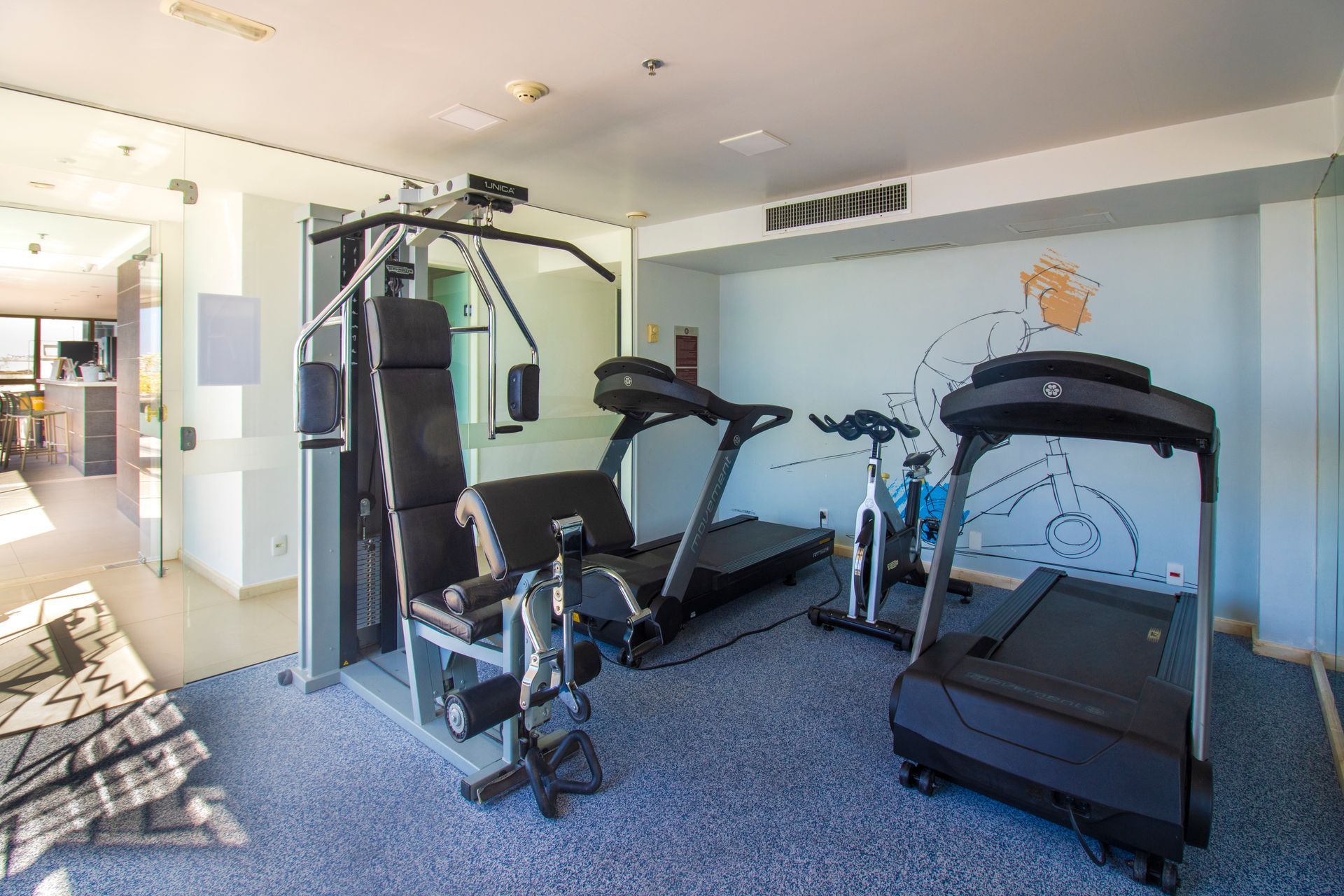 Academia em casa com esteira, máquina de musculação, banco e bicicletas ergométricas em um ambiente bem iluminado.