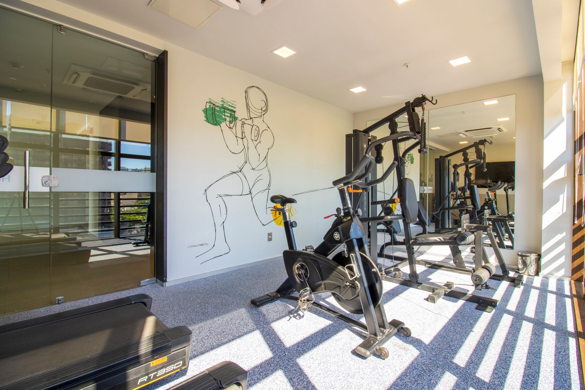 Academia moderna com bicicletas ergométricas, aparelhos de musculação e obras de arte nas paredes, em um ambiente iluminado.