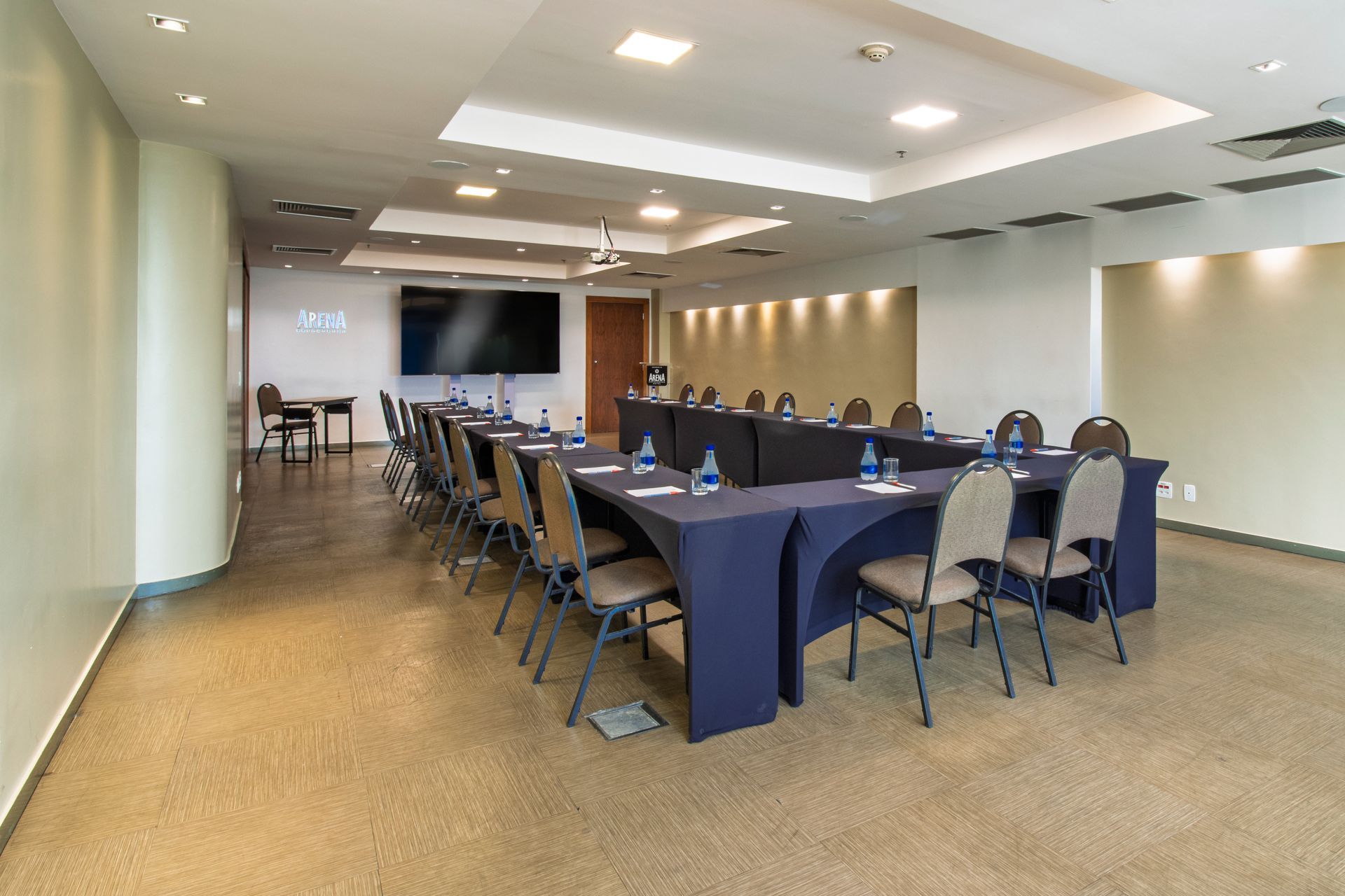 Sala de conferências com mesa comprida, cadeiras azuis e tela fixada na parede em um escritório bem iluminado.