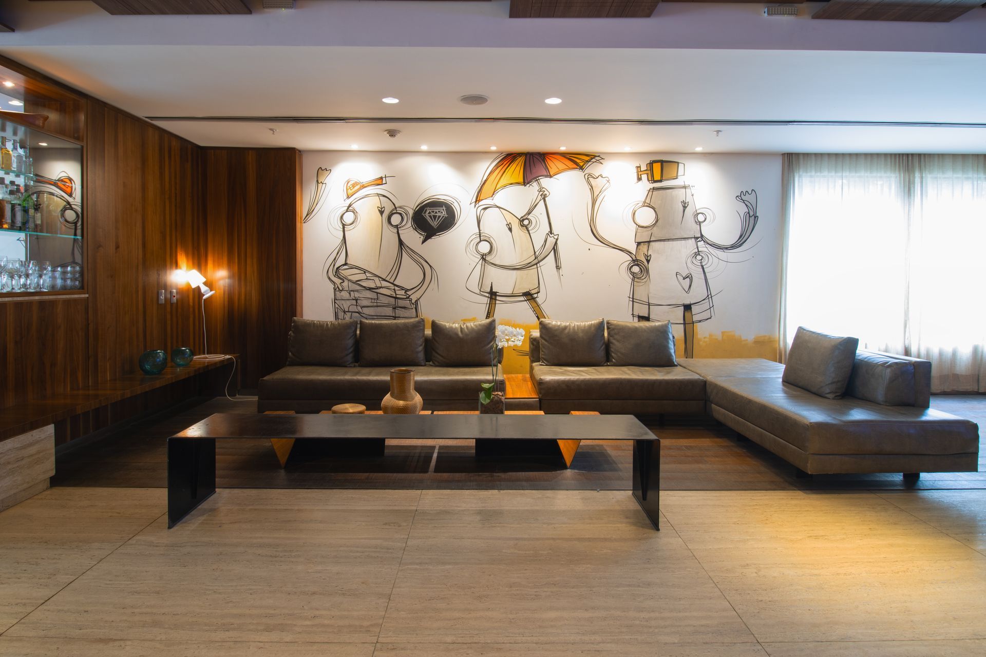 Hall de entrada de hotel moderno com sofás de couro marrom, uma mesa de centro preta e uma grande obra de arte na parede atrás deles.