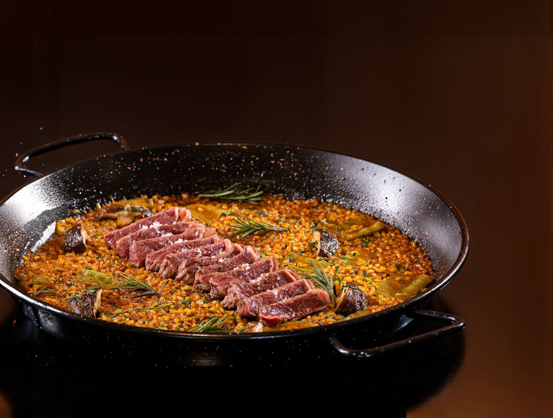 Arroz com açafrão e fatias de carne grelhada por cima, servido em uma frigideira preta.