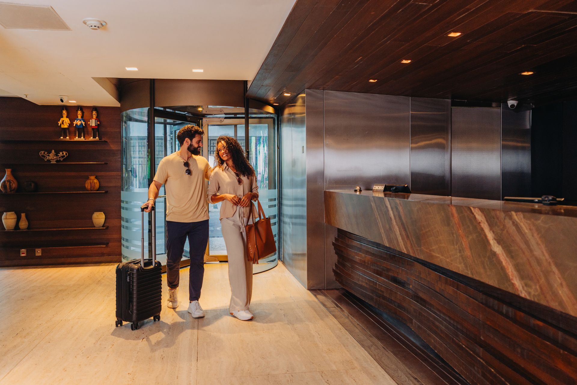 Casal com bagagem em pé no saguão de um hotel moderno, perto da recepção.