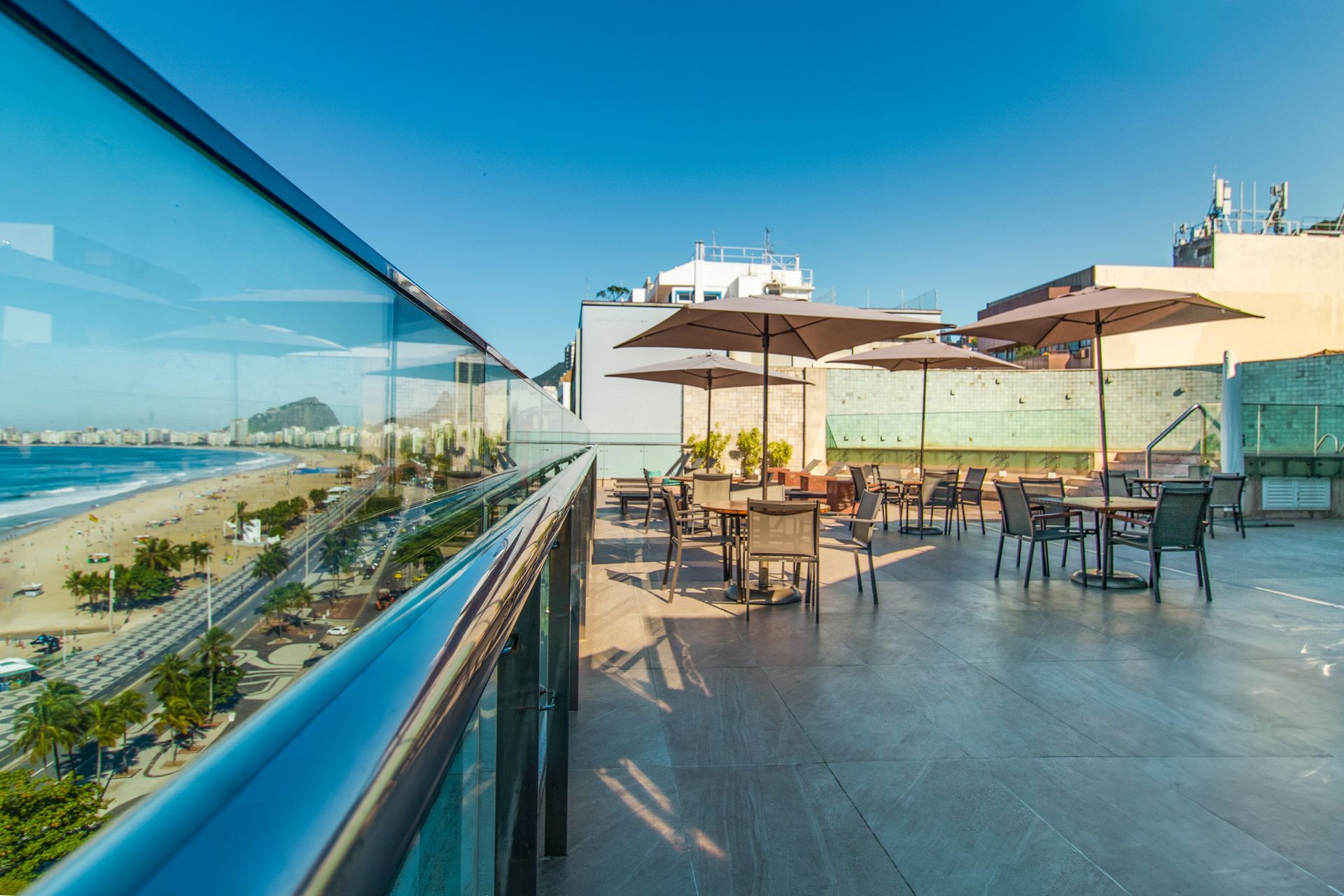 Terraço na cobertura com mesas e cadeiras com vista para a praia e o oceano em um dia ensolarado.