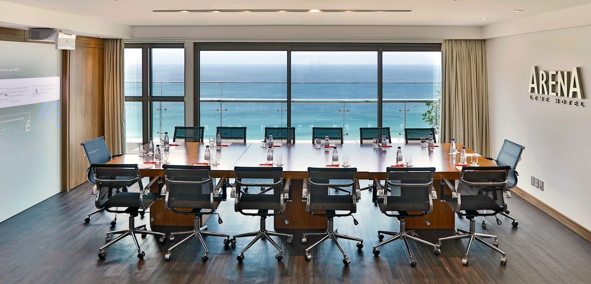 Sala de conferências moderna com fileiras de cadeiras voltadas para uma grande janela com vista para o oceano.