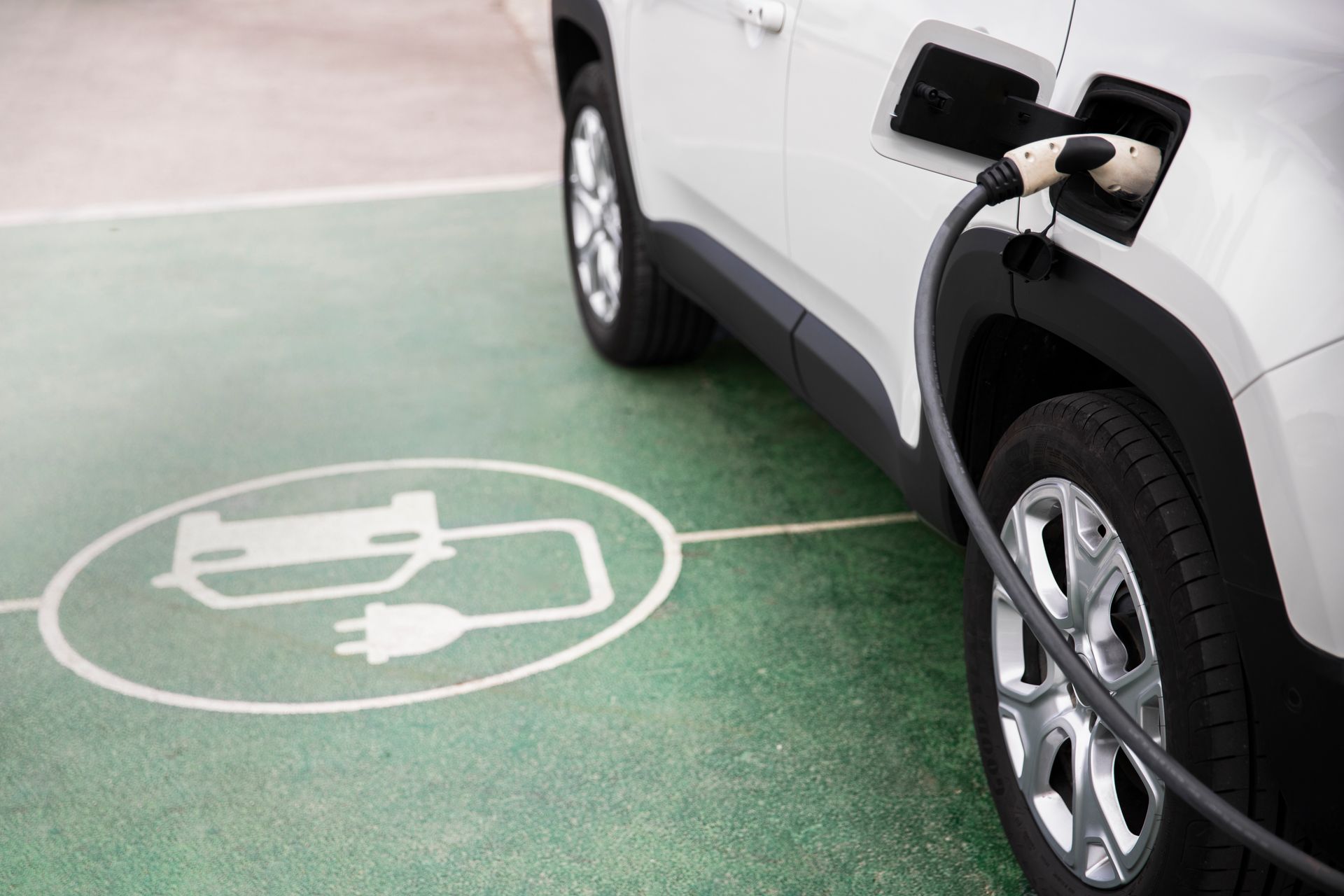 SUV elétrico branco carregando em uma vaga verde para veículos elétricos, com o símbolo do plugue marcando o chão.