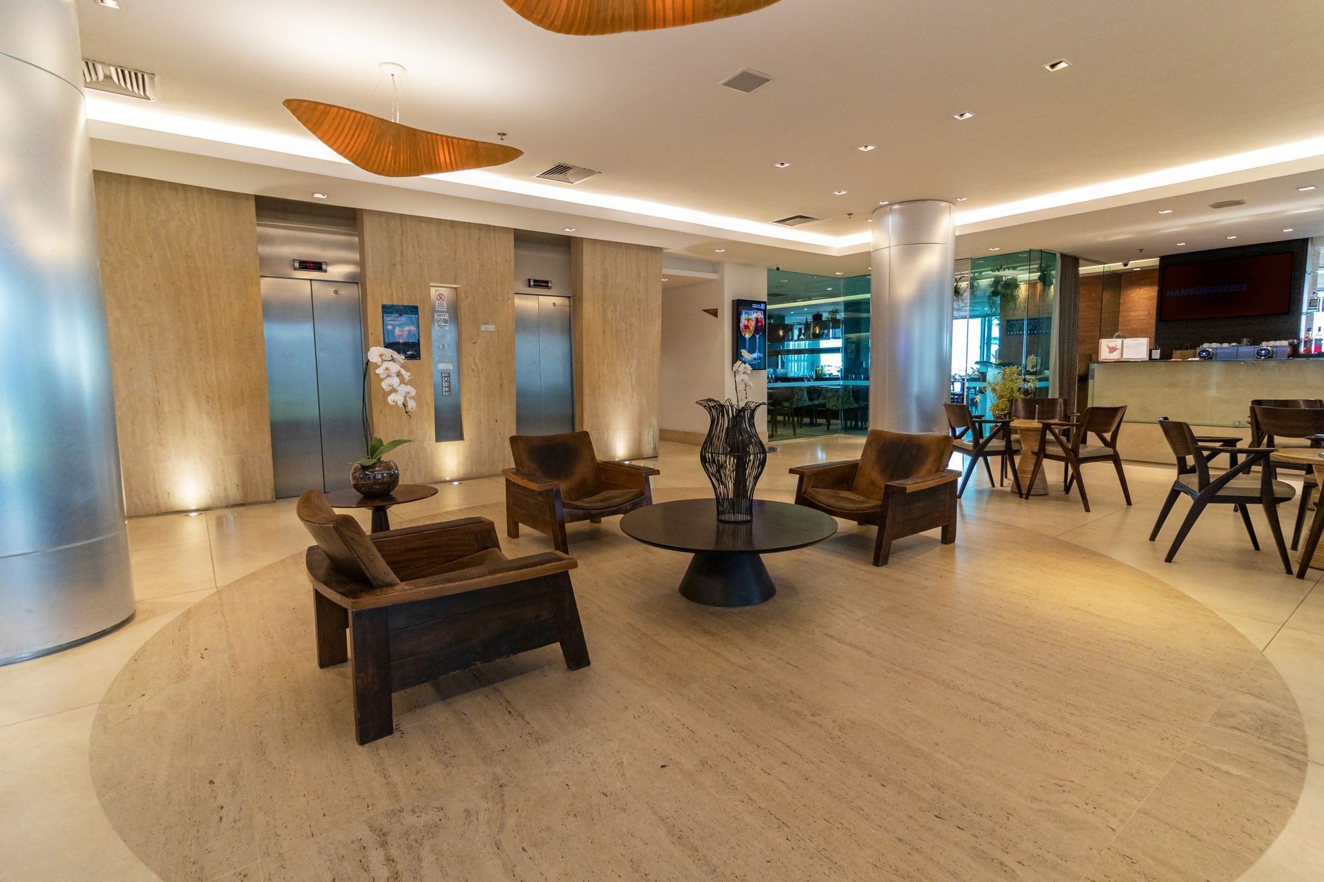 Hall de entrada moderno do hotel com área de estar, iluminação aconchegante e balcões de recepção ao fundo.