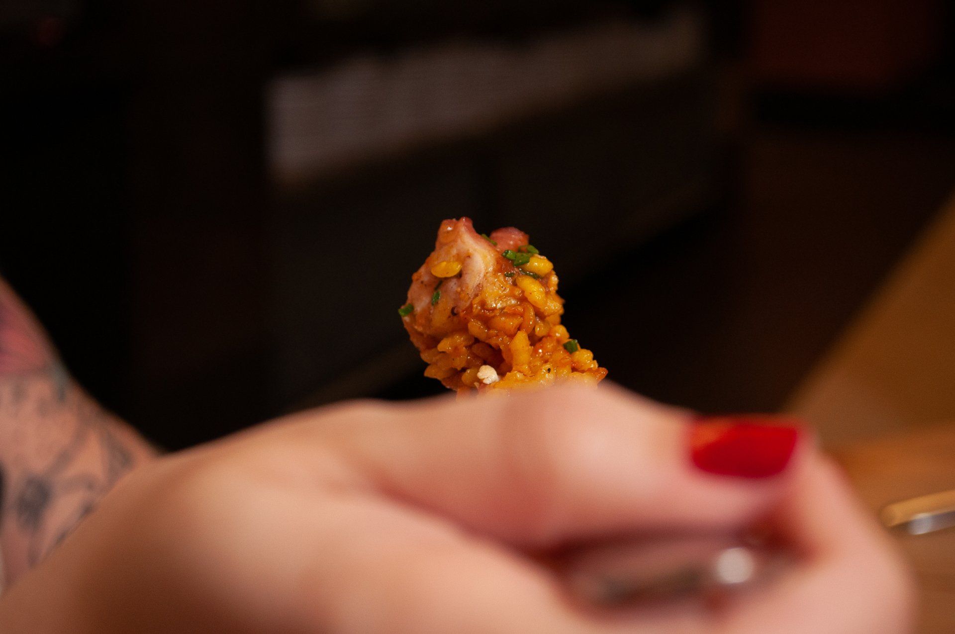 Close-up de uma mão segurando um pedaço de comida com molho e legumes picados.