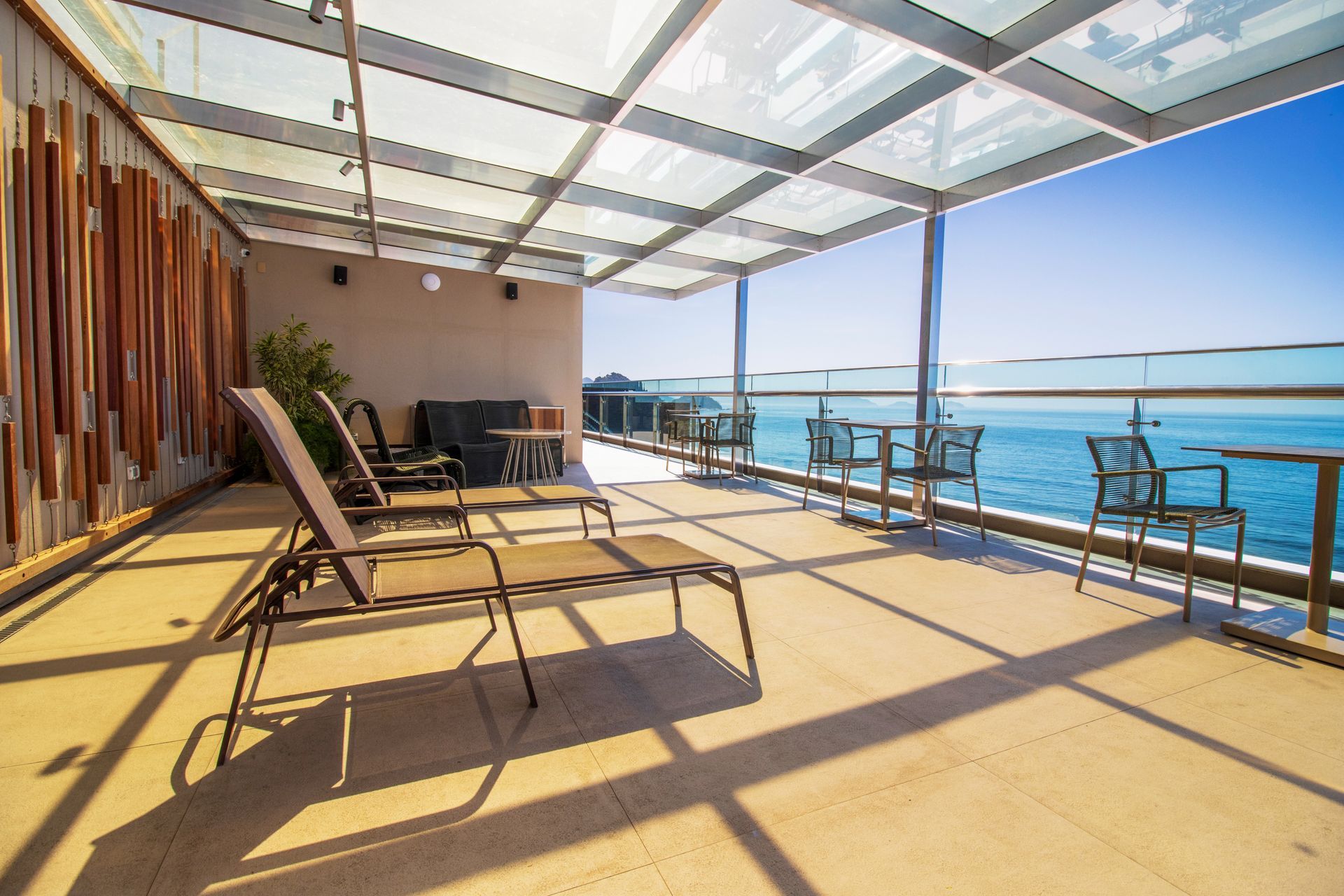 Terraço à beira-mar com espreguiçadeiras sob um toldo sombreado e vista para o mar.