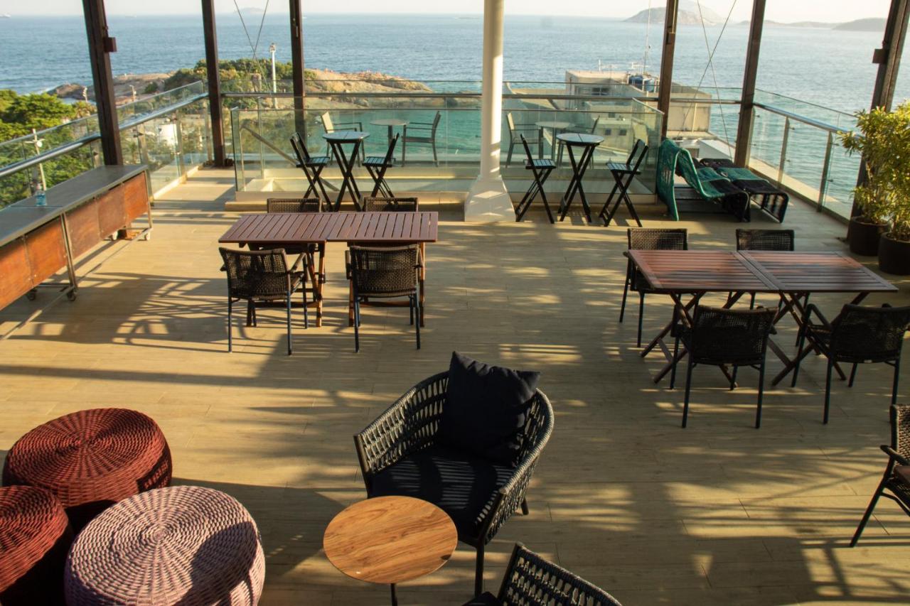 Café ao ar livre à beira-mar com mesas e cadeiras vazias em um deck de madeira com vista para o mar.