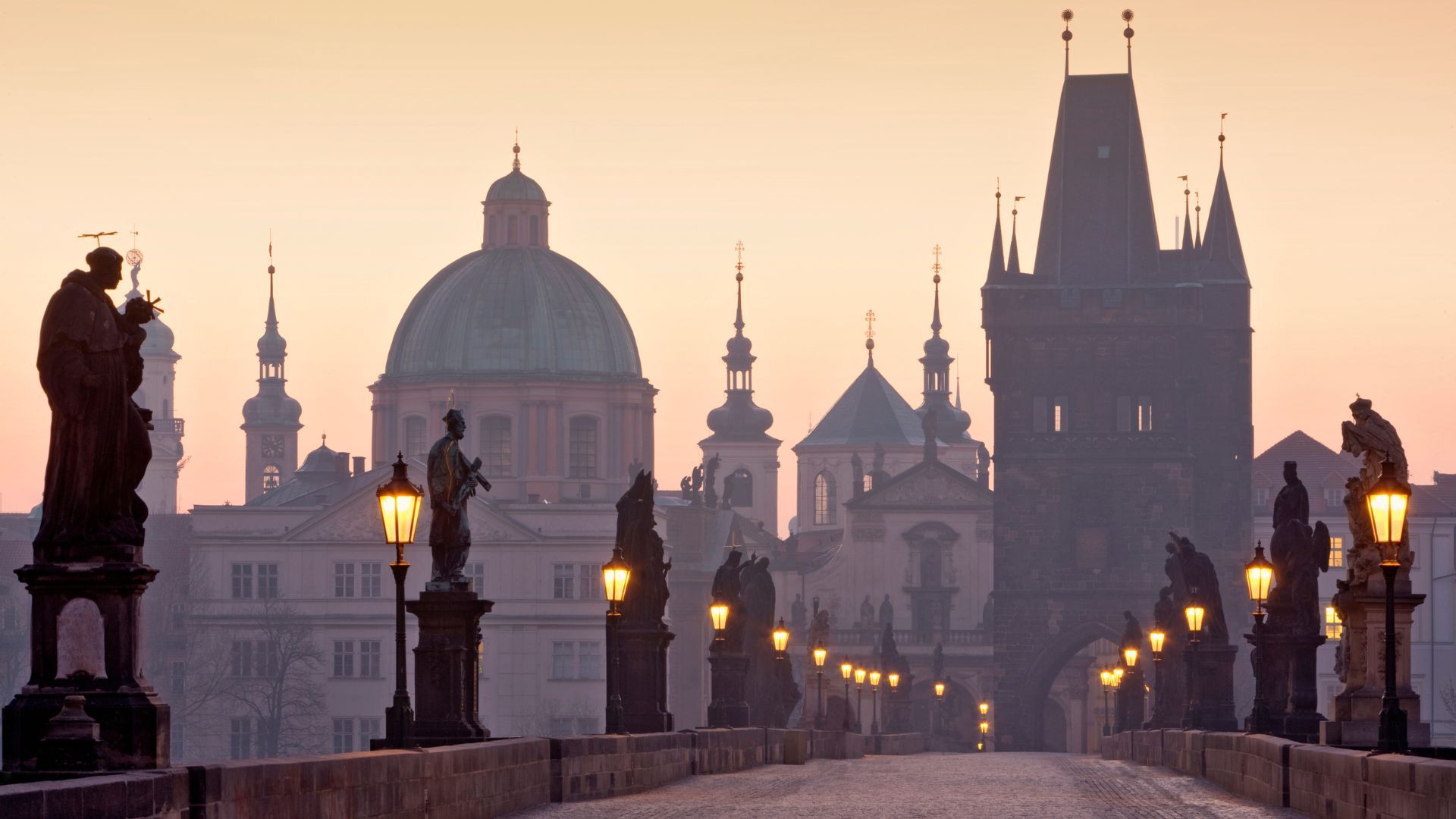 Charles Bridge in Prague at dawn; statues line the empty bridge towards the city's historic architecture.
