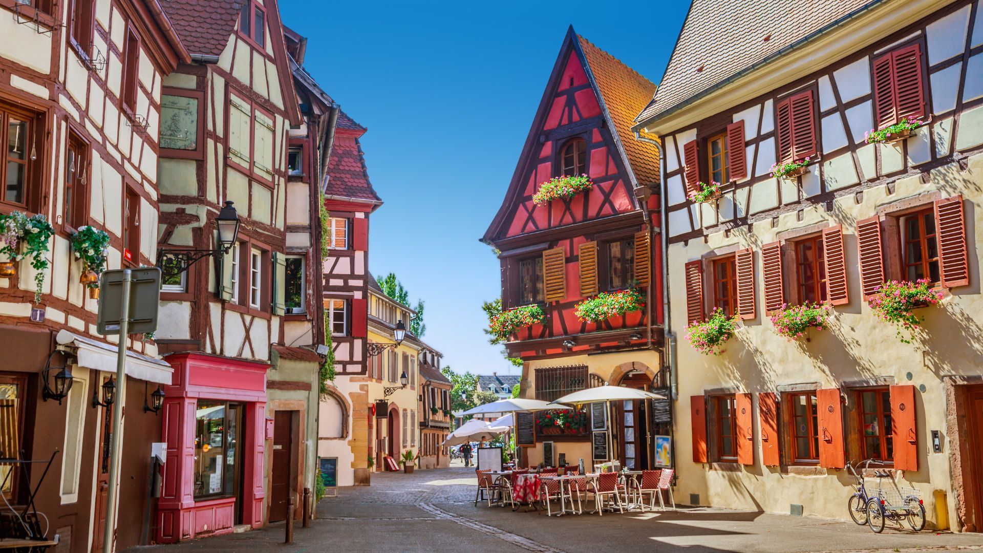 Cobblestone street lined with colorful timber-framed buildings and outdoor cafe in European town.